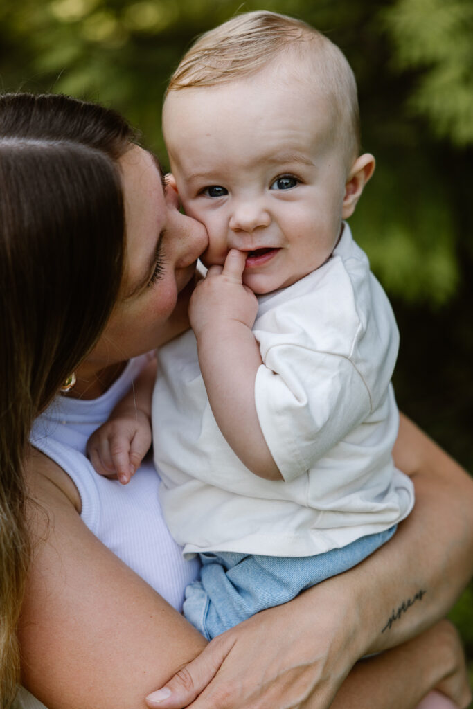 Jonge moeder houdt haar zoontje vast terwijl hij nieuwsgierig om zich heen kijkt in het groen van Trompenburg Rotterdam.