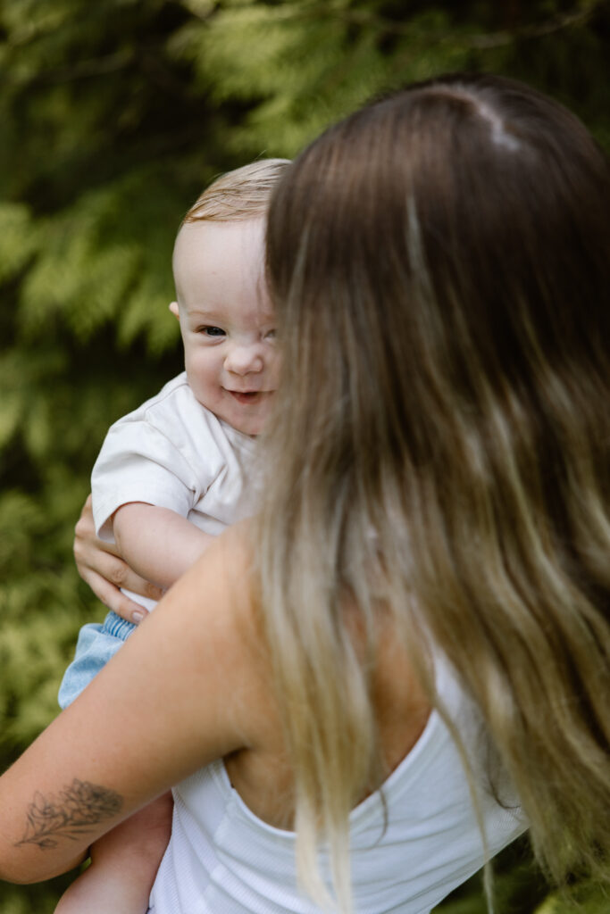 Jonge moeder houdt haar zoontje vast terwijl hij nieuwsgierig om zich heen kijkt in het groen van Trompenburg Rotterdam.