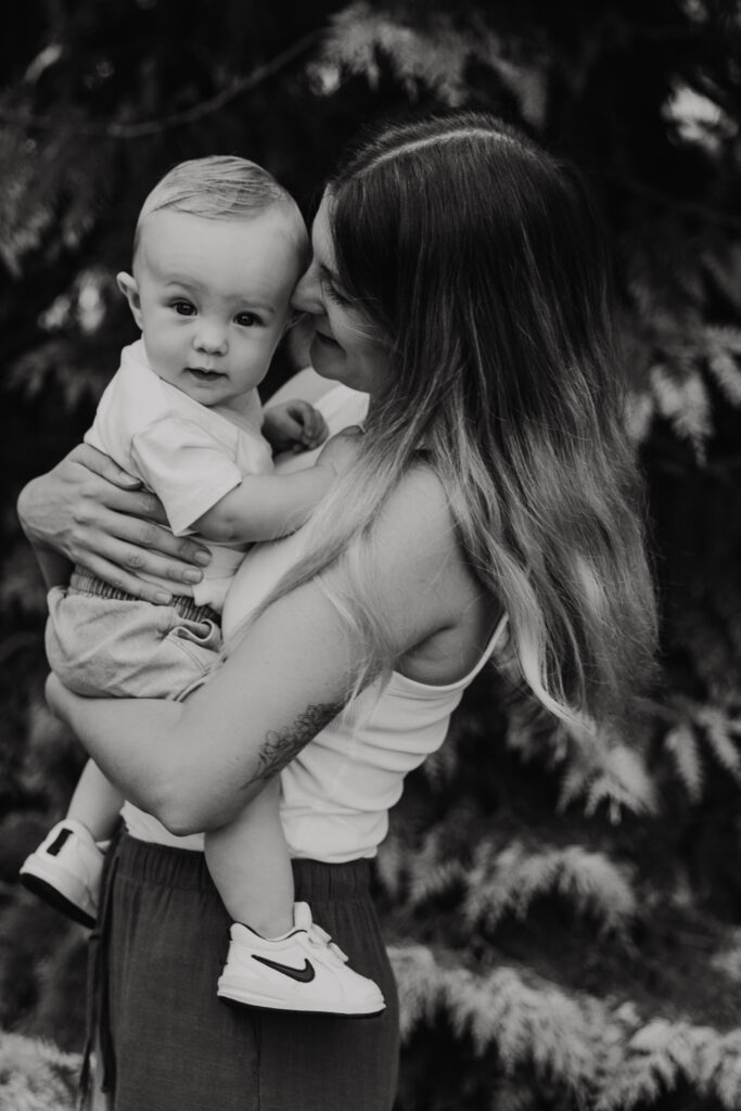 Jonge moeder houdt haar zoontje vast terwijl hij nieuwsgierig om zich heen kijkt in het groen van Trompenburg Rotterdam.
