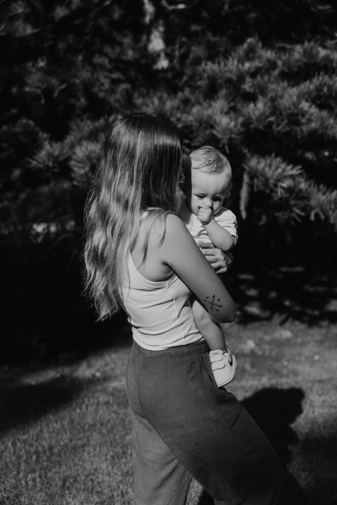 Moeder draagt haar baby terwijl ze samen door de Trompenburg Tuinen lopen.