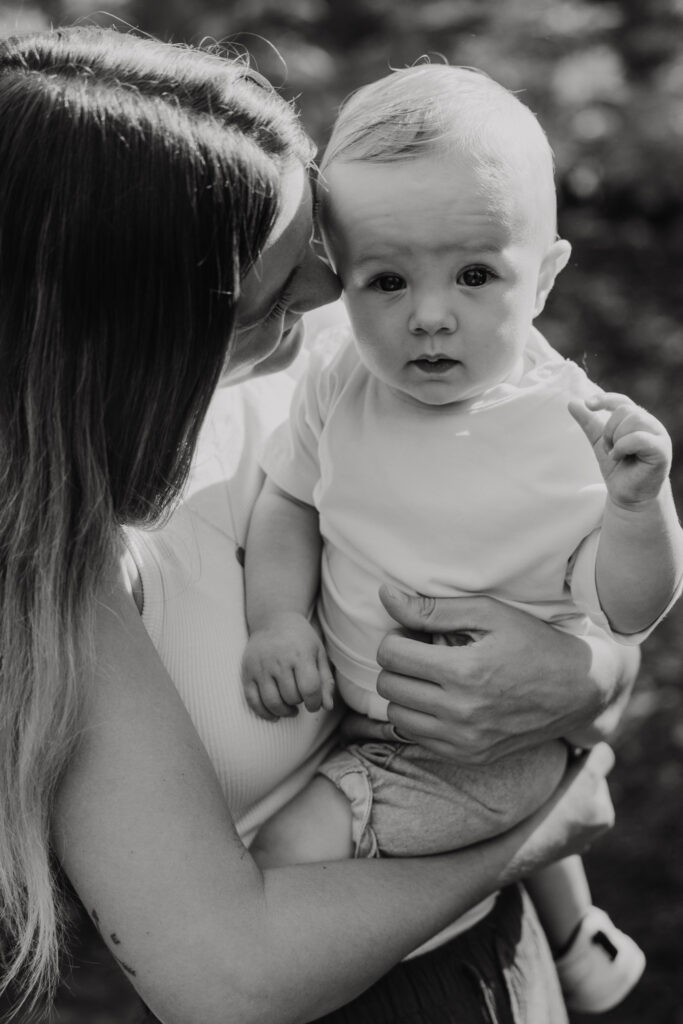 Close-up van een lachend jongetje van tien maanden dat tegen zijn moeder aanleunt tijdens een fotoshoot.