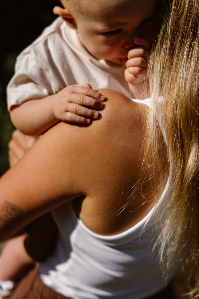 Baby verstopt zijn gezichtje in mama’s schouder tijdens een knuffelmoment.