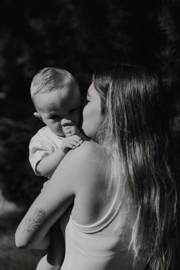 Baby verstopt zijn gezichtje in mama’s schouder tijdens een knuffelmoment.