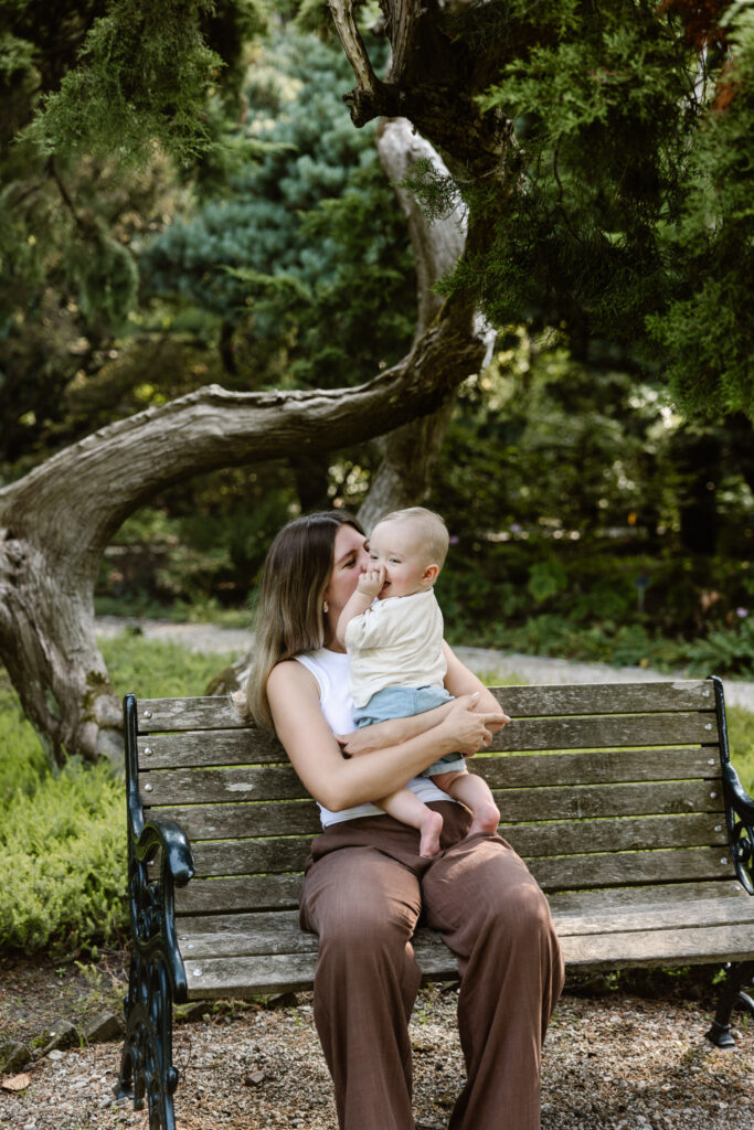 Sfeervolle lifestyle foto van moeder en kind zittend op een bankje in de tuinen.
