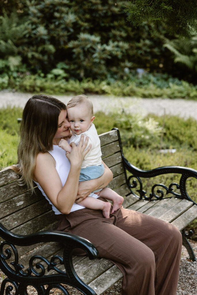 Sfeervolle lifestyle foto van moeder en kind zittend op een bankje in de tuinen.