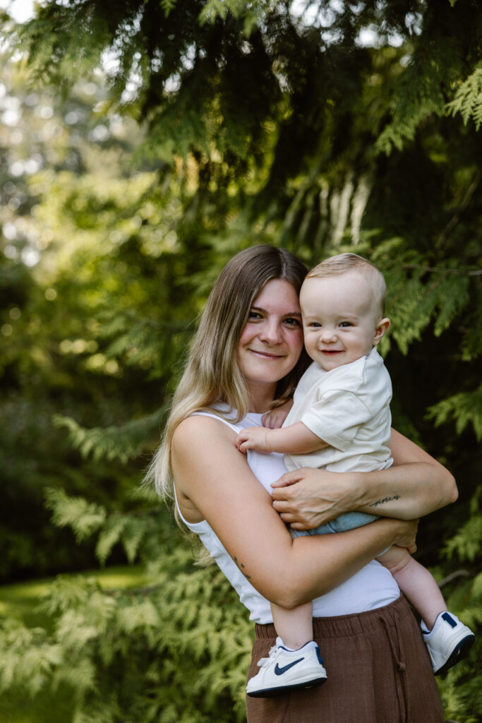 Jonge moeder houdt haar zoontje vast terwijl hij nieuwsgierig om zich heen kijkt in het groen van Trompenburg Rotterdam.