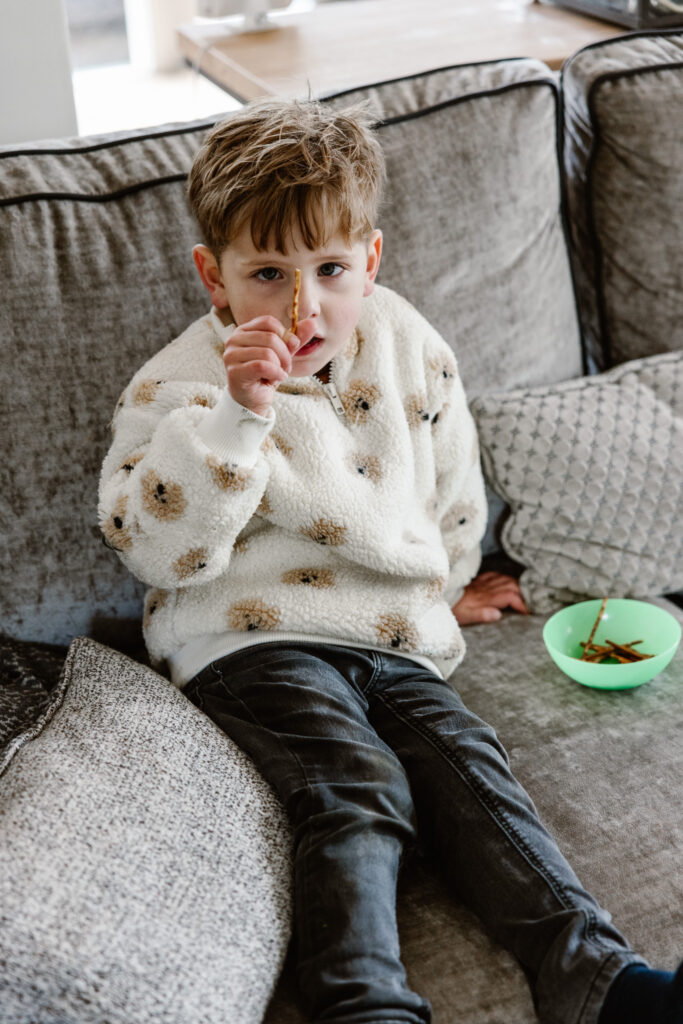 Twee kinderen springen op de bank bij opa en oma tijdens een huiselijke familieshoot.