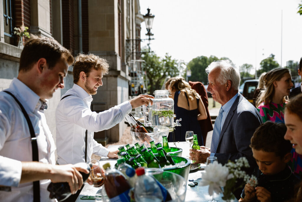 Gasten genieten van champagne voor het Muntgebouw tijdens een zomerse bruiloft in Utrecht.